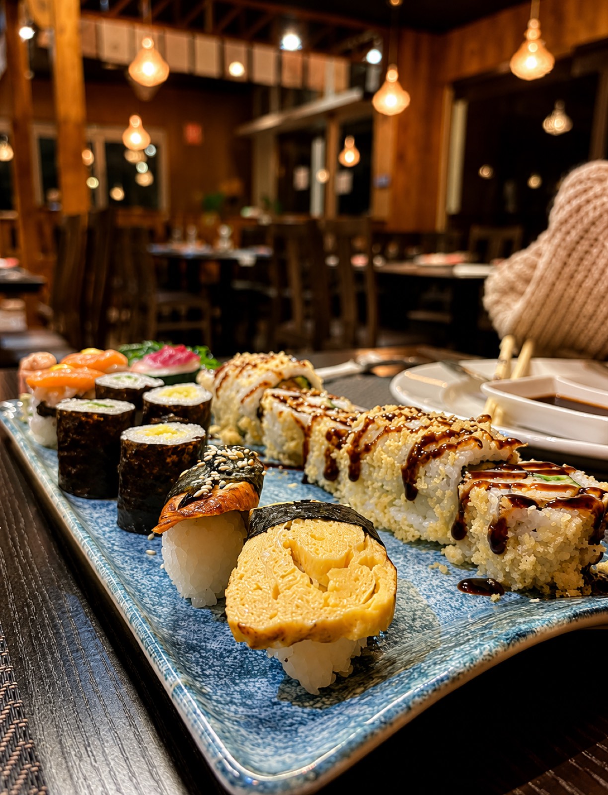Bandeja de sushi recién preparada en primer plano, con el comedor de Yamato Gandía de fondo